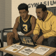 High school basketball player reviewing college recruiting materials with parent in a gym lobby