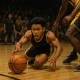 Youth basketball player diving for the ball in a competitive one-on-one game wearing black and yellow PSB uniform.