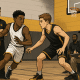 Young basketball players showcasing skills in a camp setting with coaches observing and scouts taking notes.