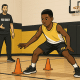Youth basketball player practicing footwork drills in a gym with cones and a coach watching