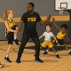 Young basketball players performing dynamic stretches on a court with coach supervision, in PSB brand colors.