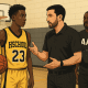 High school and AAU basketball coaches talking with a youth player in the gym, representing collaboration in youth basketball development.