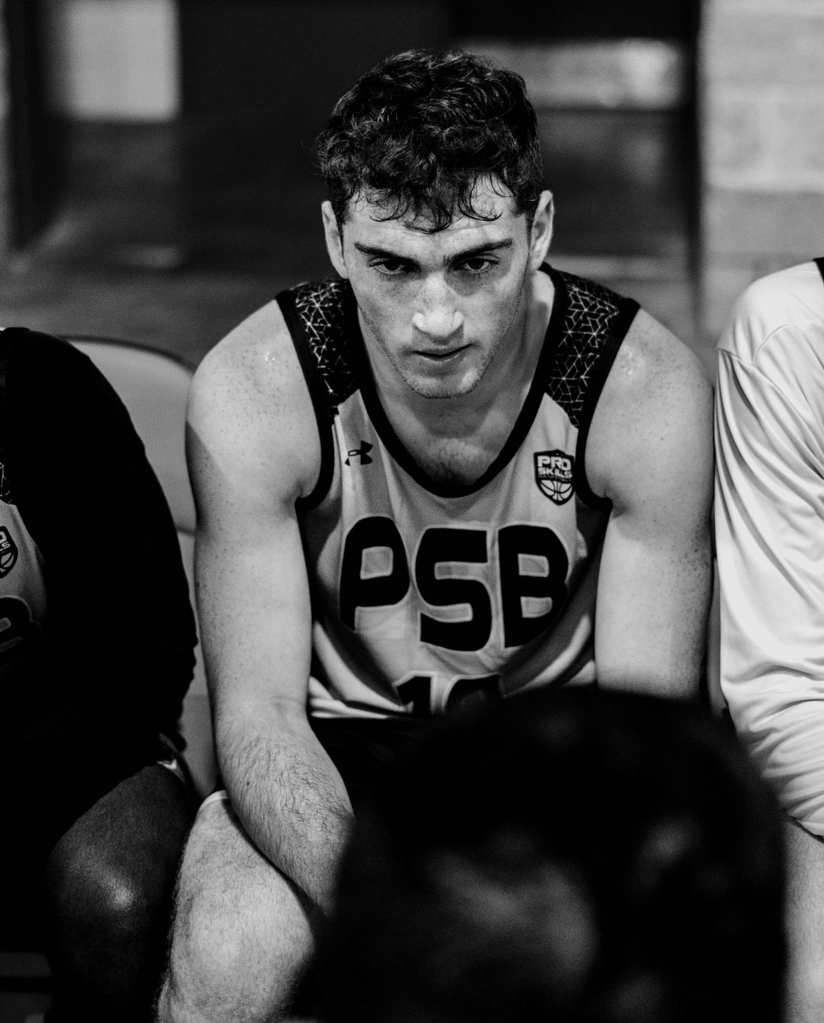 Focused youth basketball player watching from the bench at a tournament, PSB player in dark jersey
