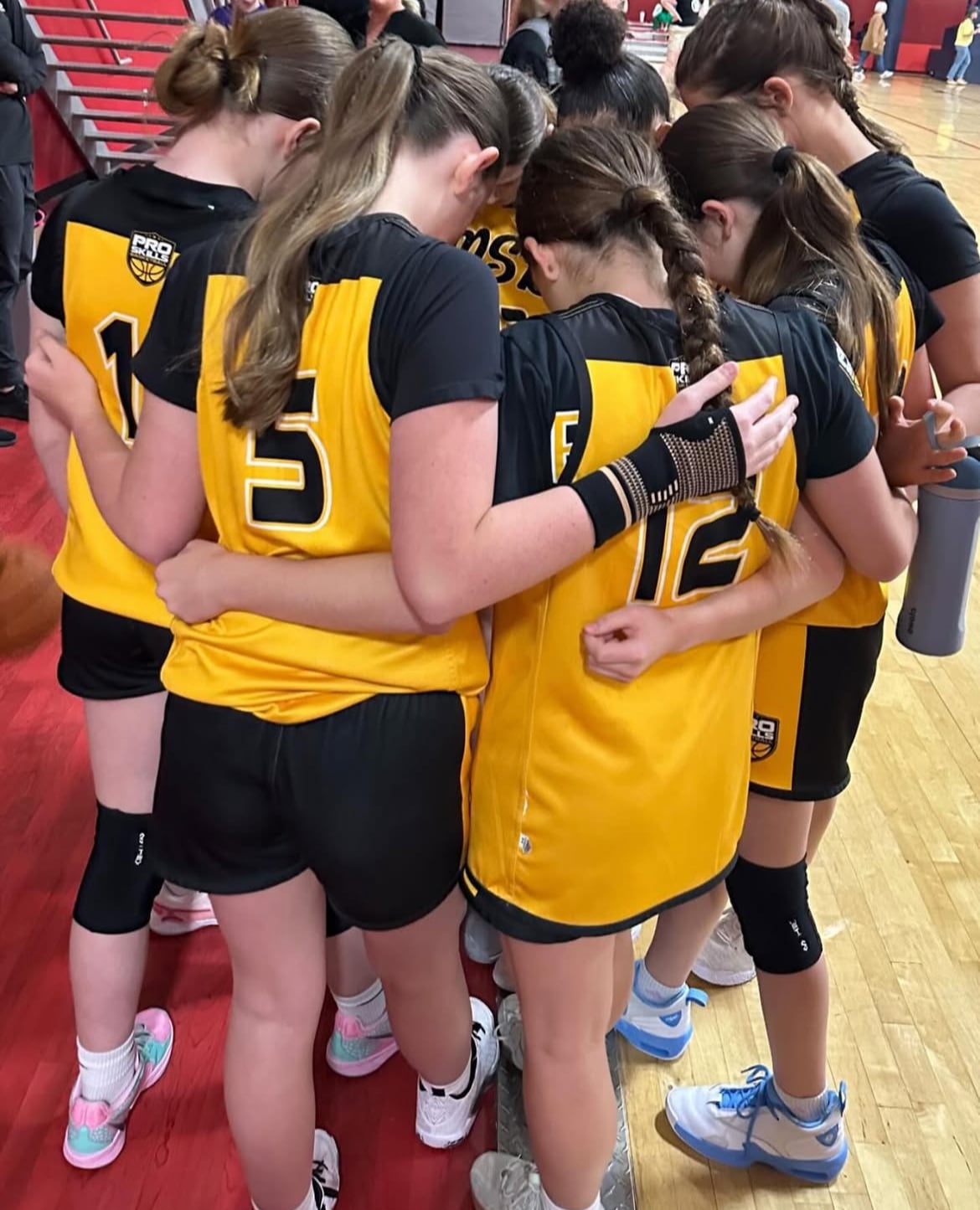 Girls AAU basketball team in a sideline huddle with their coach