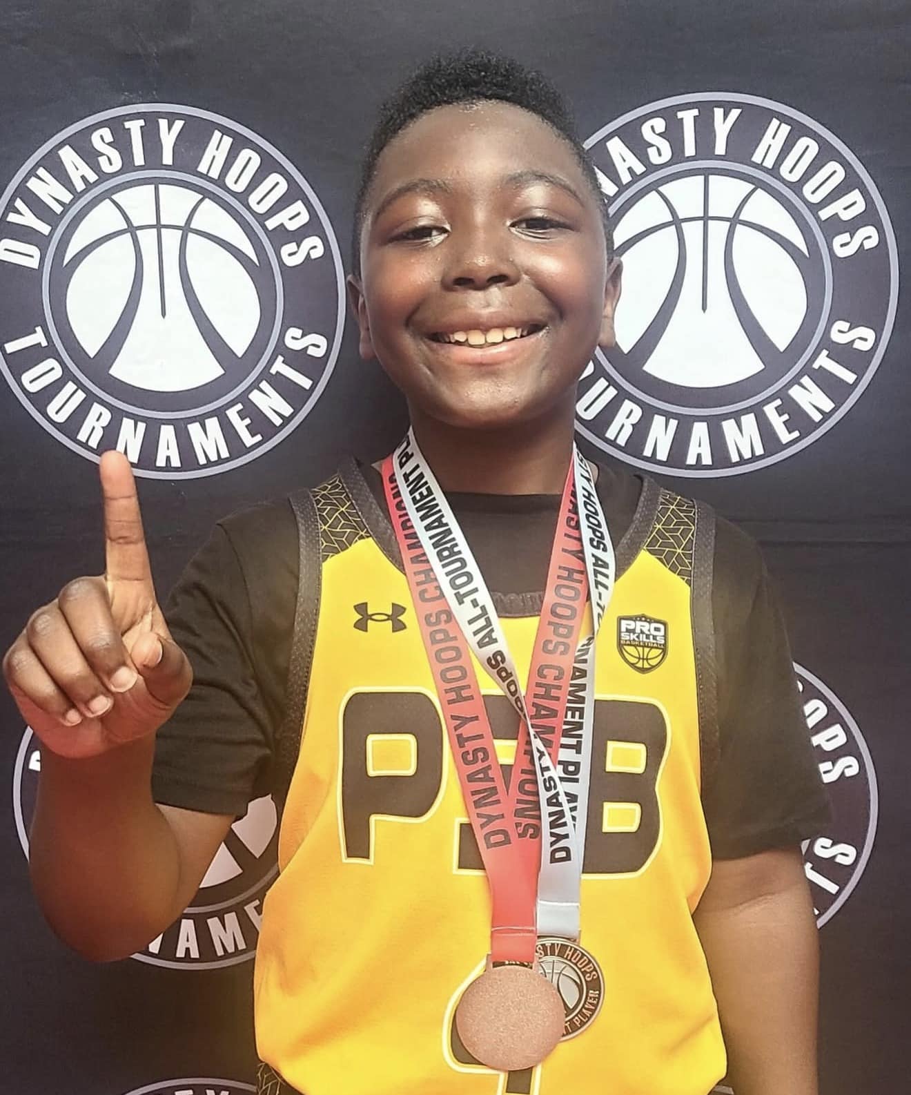 A smiling 3rd grade basketball player holding up one finger and wearing a tournament medal